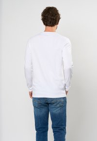 T-shirt bianco a maniche lunghe con scollatura rotonda, abbinato a jeans in denim blu. La maglietta ha una texture liscia e maniche aderenti.