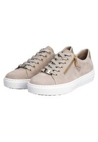 Des sneakers en suède beige présentent une semelle en caoutchouc blanc, des lacets gris et une fermeture éclair dorée sur le côté. Design plat avec un bout arrondi.