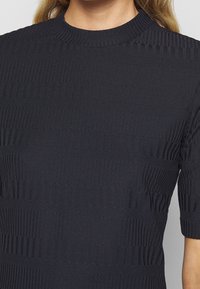 Sweter dzianinowy w ciemnym granacie z teksturowanymi poziomymi paskami. Krótkie rękawy, prążkowany okrągły dekolt i dopasowany krój.