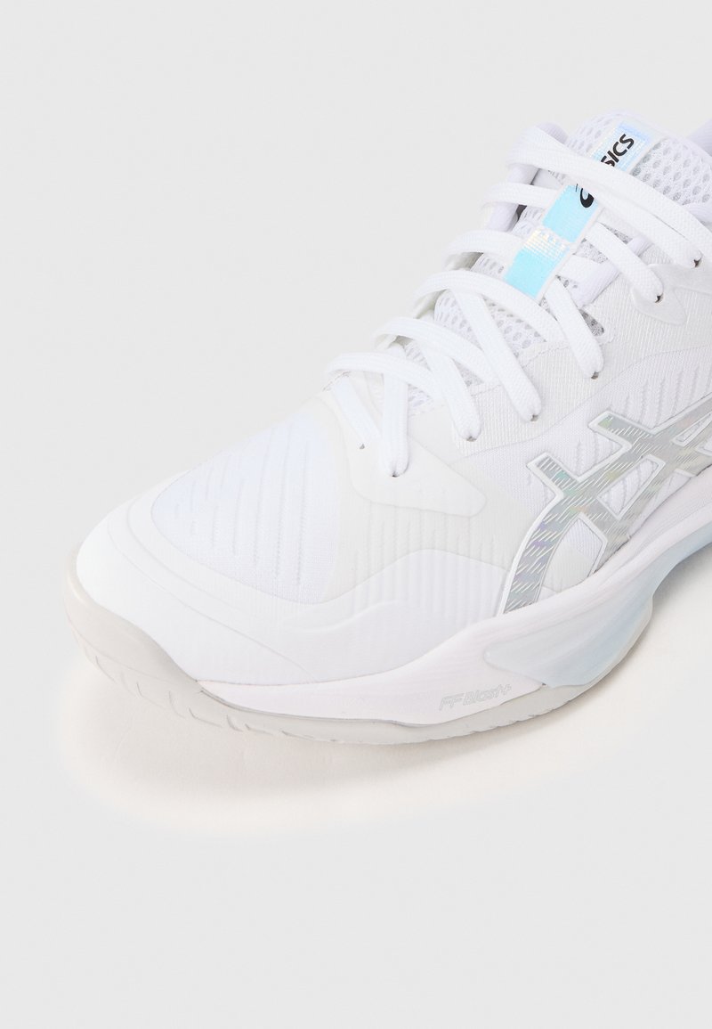 Chaussure de sport blanche avec une tige en mesh, des panneaux texturés et un logo argenté réfléchissant. Semelle en caoutchouc avec des accents subtils et un système de laçage.