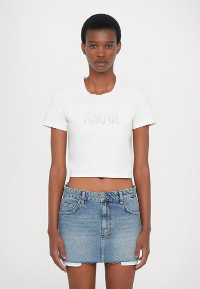 Witte cropped t-shirt met een ronde halslijn en korte mouwen, met een zilveren logo aan de voorkant. Gecombineerd met een blauwe denim mini-jurk.