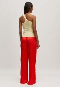 Beige top met één schouder, gecombineerd met rode geplooide wijde broek. De top is nauwsluitend, terwijl de broek een glanzende textuur en een losse silhoeet heeft.