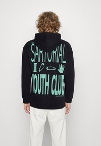 Crna dukserica s velikim mint zelenim grafičkim natpisom "SARTORIAL YOUTH CLUB" i ikonama na leđima; pamuk s opuštenim krojem.