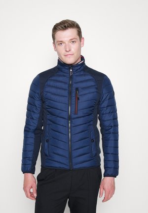 Navyblaue gesteppte Jacke mit hohem Kragen, kontrastierenden Seitenpaneelen, Reißverschluss und einer Reißverschlusstasche auf der Brust. Textil mit strukturierter Oberfläche und glatter Verarbeitung.