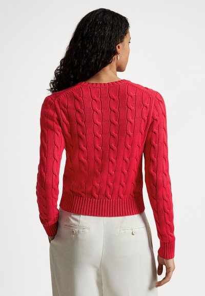 Pulover roșu cu model în torsadă, cu mâneci lungi și tiv striat, cu un model texturat. Modelul poartă pantaloni deschiși la culoare.