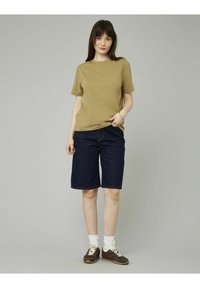 T-shirt vert olive, à manches courtes, associé à un short en jean bleu marine. Des chaussettes blanches à mi-mollet et des baskets brunes complètent la tenue. Design simple.