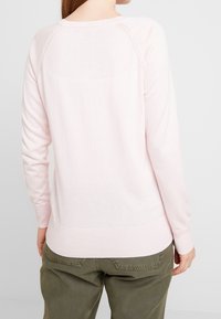 Světle růžový svetr s dlouhým rukávem, s žebrovanými manžetami a lemem, s kulatým výstřihem a jemným trojúhelníkovým pleteným detailem na ramenou.