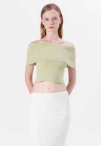 Top corto de canalé sin mangas en verde claro, combinado con una falda texturizada blanca. La tela suave y el diseño ajustado realzan la cintura.