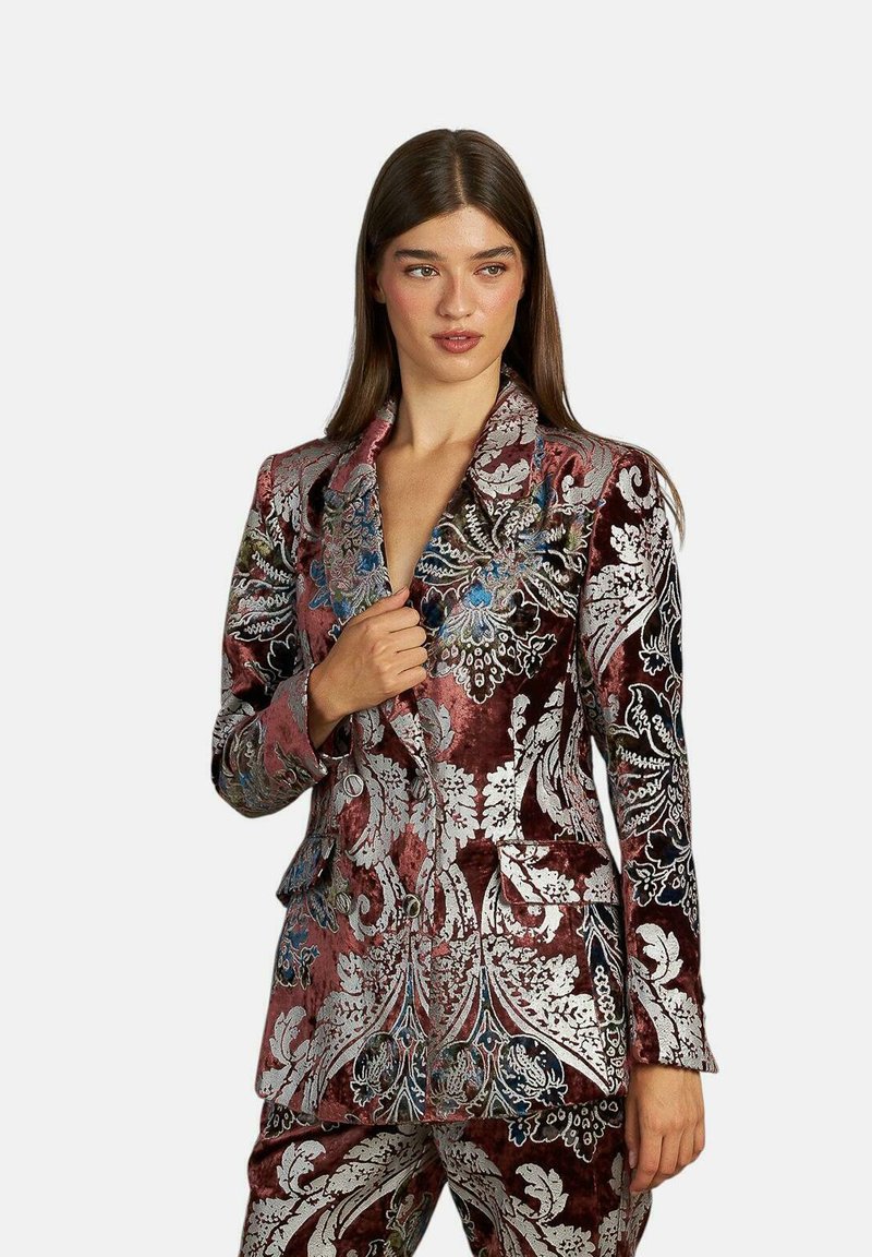 Traje de terciopelo en burdeos con intrincados bordados florales plateados. Diseño de doble botonadura con solapas con muescas y dos bolsillos.
