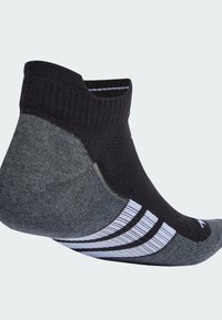 Calcetín deportivo negro y gris con un diseño de corte bajo, que presenta una parte superior de punto texturizado, un talón reforzado y tres franjas blancas a lo largo del costado.
