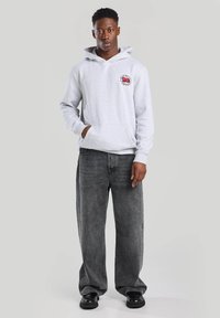 Gray hoodie with a front pocket, featuring a small red graphic on the chest, paired with loose-fitting black jeans and chunky black shoes.