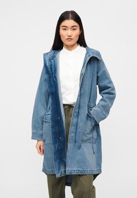 Παρκά από τζιν ύφασμα με δίχρωμο σχεδιασμό, σε ανοιχτό και σκούρο μπλε. Διαθέτει κουκούλα, κουμπιά κλιπς και δύο μπροστινές τσέπες.