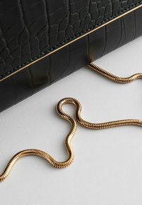 Clutch in pelle nera con stampa a coccodrillo, dotata di tracolla in catena dorata, caratterizzata da una texture liscia e da una forma rettangolare elegante.