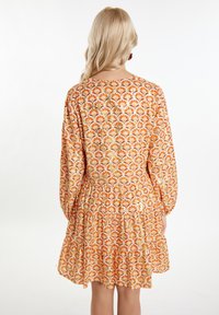 Rochie cu imprimeu floral în nuanțe de portocaliu și galben, cu mâneci lungi și bufante și fustă cu volane. Material ușor, cu o textură netedă.
