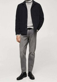 Giacca in misto lana scura con quattro bottoni e taschino, abbinata a un dolcevita grigio chiaro in maglia e jeans grigi, completata da stivali neri.