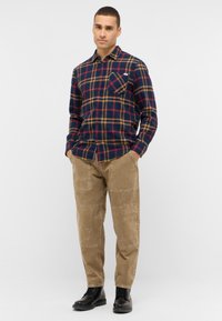 Marineblauw geruit flanellen overhemd met rode en beige accenten, enkele borstzak; gecombineerd met beige gestructureerde broek en zwarte veterlaarzen.