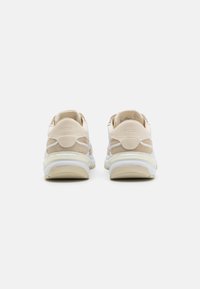Sneakers caratterizzati da una combinazione di materiali beige e bianchi, texture liscia, forma arrotondata e un delicato marchio sul tallone.