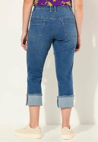 Džínové kalhoty ve středně modré barvě s ohrnutými nohavicemi, s dvěma zadními kapsami a rovný střihem. V kombinaci se světlými teniskami.