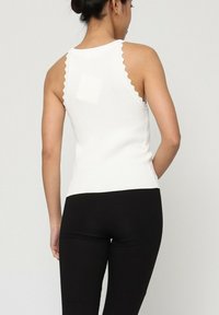 Débardeur blanc à côtes avec un détail de décolleté festonné, coupe ajustée et texture douce, associé à des leggings noirs à côtes.