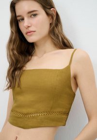 Olijfgroen cropped top met dunne bandjes, heeft een vierkante halslijn en een decoratief uitsnijdpatroon langs de zoom. Gemaakt van lichte stof.