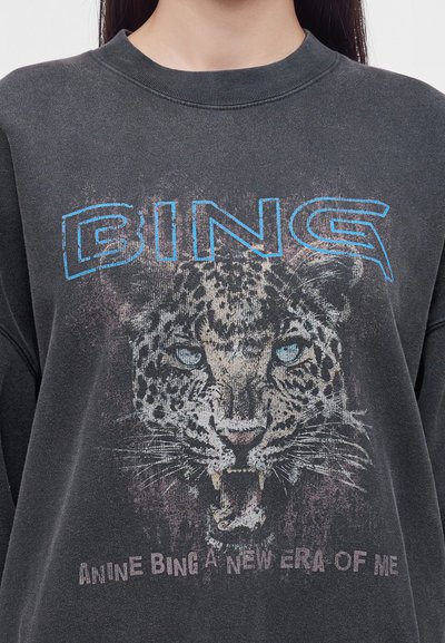 Sweat-shirt gris foncé avec un grand graphisme d'un visage de léopard qui grogne et un texte bleu indiquant "BING" au-dessus et "ANNIE BING A NEW ERA OF ME" en dessous.