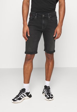 Pantaloncini in denim nero con risvolti, caratterizzati da un classico design a cinque tasche e ferramenta color argento, indossati con scarpe da ginnastica nere e bianche.