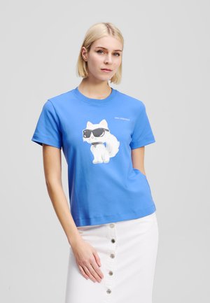 Tricou din bumbac albastru, cu imprimeu reprezentând o pisică albă purtând ochelari de soare. Mâneci scurte, guler rotund și o croială lejeră. Eticheta brandului este vizibilă.