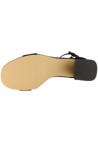 Semelle de sandale avec fond lisse beige et talon carré noir texturé, vue de dessous d'une chaussure noire à brides.