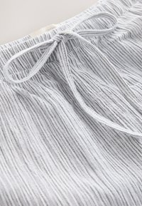 Gros plan d’un tissu rayé gris et blanc avec un cordon noué et une ceinture élastique visible sur un vêtement doux.