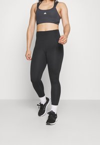 Czarne legginsy sportowe z wysokim stanem, w połączeniu z czarnym stanikiem sportowym z szerokimi ramiączkami i małym logo z przodu.