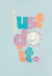 T-shirt azzurro con testo multicolore "just do it" decorato da motivi a strisce e una grafica di un sorriso circolare con raggi di sole.