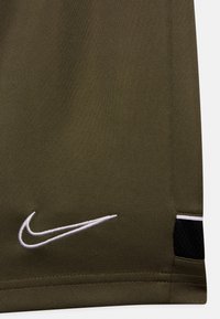 Tissu vert olive avec le logo Nike en broderie blanche près de l'ourlet et un petit détail en maille noire avec une bordure blanche sur le côté.
