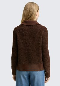 Bruine, gestructureerde trui met een geribbelde kraag en zoom, met een pluizig oppervlak en lange mouwen, gedragen over een blauwe spijkerbroek.