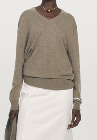 Pull col en V en mélange de laine beige, coupe décontractée avec ourlet et poignets côtelés, associé à une jupe en satin blanc. Design simple, sans ornement.