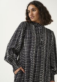 Rochie cu un model alb-negru, cu guler înalt, mâneci bufante, material texturat și detalii cu nasturi la gât.