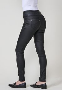 Jeans ajustados negros con una cinturilla alta, hechos de un tejido suave y elástico. Presentan dos bolsillos traseros con detalles de costura sutil.