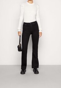 Haut blanc à manches longues côtelé avec épaules bouffantes, assorti à un jean noir évasé taille haute et des chaussures noires épaisses. Petit sac noir inclus.