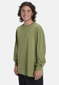 Langärmliges, olivgrünes Baumwoll-T-Shirt mit Rundhalsausschnitt und gesticktem Logo auf der Brust. Bietet eine lockere Passform und gerippte Bündchen.