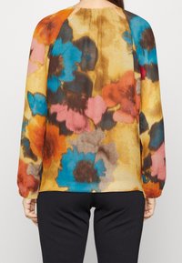 Chemisier floral multicolore présentant un mélange de nuances orange, bleu, rose et marron sur un fond crème, avec des manches longues et un col froncé.