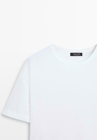 T-shirt blanc à manches courtes et col rond, tissu lisse, avec une petite étiquette noire au dos du col affichant le nom de la marque.