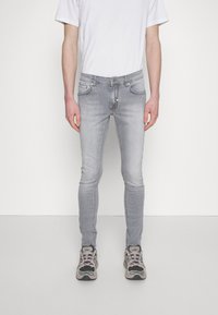 Vaqueros ajustados grises de mezclilla con cremallera, bolsillos frontales y una textura desgastada. Combinados con zapatillas negras y grises.