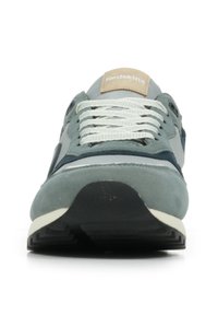 Baskets vertes avec tige en daim et en mesh, lacets blancs, étiquette de logo sur la languette et semelle en caoutchouc noire. Présente un design texturé et des matériaux superposés.