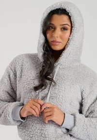 Sudadera con capucha de color gris claro, fabricada en un material aterciopelado y esponjoso. Presenta una textura suave, cordones y puños acanalados en un gris contrastante.