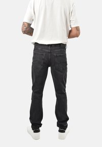 Jeans in denim nero con taglio a gamba dritta, cinque tasche e leggero effetto sbiadito. Abbinati a una maglietta bianca semplice e scarpe da ginnastica bianche.