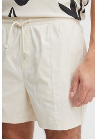 Light beige shorts made of soft fabric with an elastic waistband and drawstring. Features front pockets and a relaxed fit.