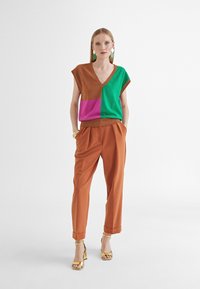 Wielokolorowy sweter (brązowy, zielony, różowy) z dekoltem w serek i bez rękawów, w połączeniu z jasnobrązowymi spodniami plisowanymi i złotymi sandałami.