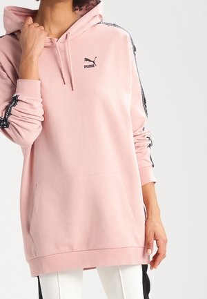 Haut à capuche rose en tissu doux, avec une poche kangourou, une capuche, et des bandes noires sur les côtes avec un logo sur la poitrine.