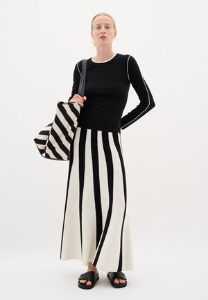 Haut noir à manches longues avec des accents blancs, associé à une jupe rayée noir et blanc et des sandales à glissière noires. Inclut un sac fourre-tout rayé.