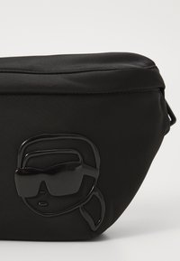 Black pouch made of smooth fabric, featuring a raised, glossy logo of a face with sunglasses. Shape is rounded with a zipper closure.