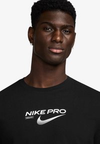Svart Nike Pro t-skjorte laget av bomull, med en hvit logo og tekst i fet skrift på brystet, med rund hals.